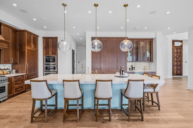 kitchen with a large island with sink, light wood-type flooring, stainless steel appliances, and pendant lighting