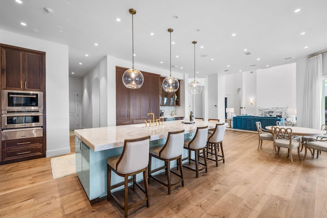 kitchen featuring light stone countertops, light wood-type flooring, decorative light fixtures, a breakfast bar area, and a large island