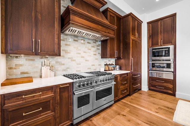 kitchen with premium range hood, tasteful backsplash, light hardwood / wood-style flooring, and appliances with stainless steel finishes