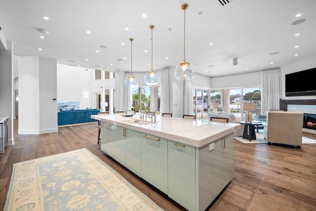 kitchen with hardwood / wood-style floors, pendant lighting, a large island with sink, sink, and light stone counters