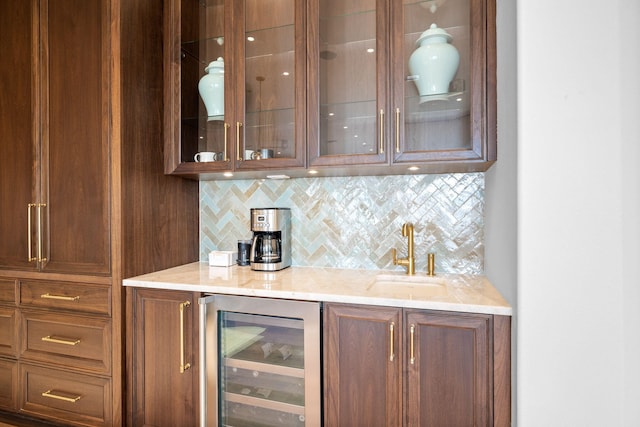 bar featuring decorative backsplash, light stone counters, beverage cooler, and sink