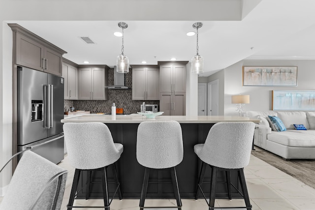 kitchen featuring a breakfast bar area, high end refrigerator, hanging light fixtures, and wall chimney range hood