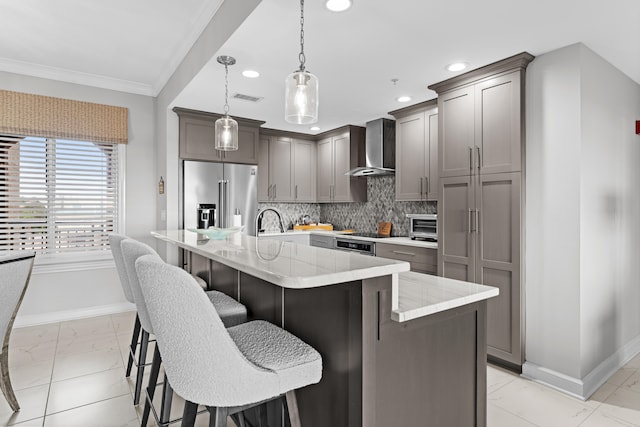 kitchen with a center island with sink, a kitchen breakfast bar, wall chimney range hood, decorative light fixtures, and high end fridge