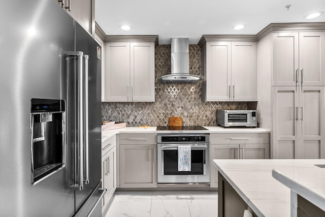 kitchen featuring decorative backsplash, stainless steel appliances, gray cabinets, and wall chimney exhaust hood