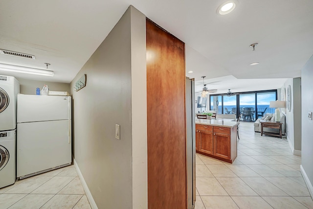 clothes washing area with stacked washer / drying machine, ceiling fan, and light tile patterned floors