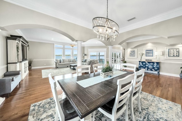 dining room featuring a chandelier, ornate columns, dark wood-type flooring, and ornamental molding