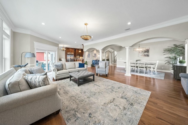 living room featuring a notable chandelier, dark hardwood / wood-style floors, ornate columns, and ornamental molding