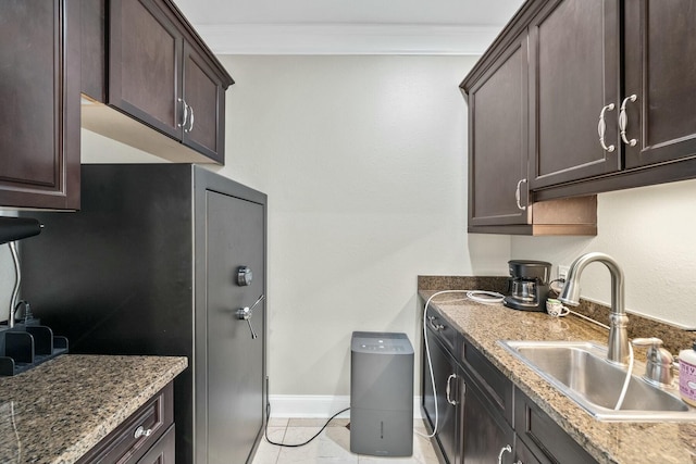 kitchen featuring dark brown cabinetry, sink, crown molding, stone countertops, and light tile patterned floors