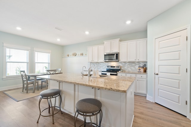 kitchen with white cabinets, light hardwood / wood-style floors, stainless steel appliances, and an island with sink