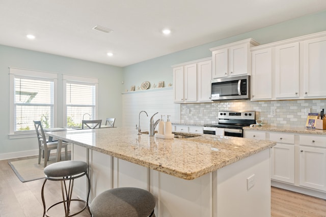 kitchen featuring a center island with sink, white cabinets, stainless steel appliances, and light wood-type flooring