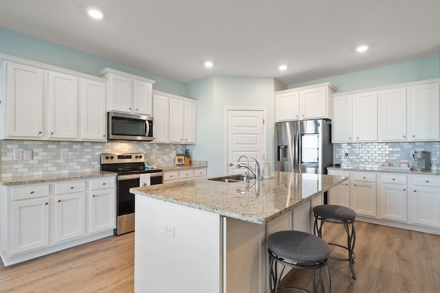 kitchen featuring white cabinets, a center island with sink, decorative backsplash, light hardwood / wood-style floors, and stainless steel appliances