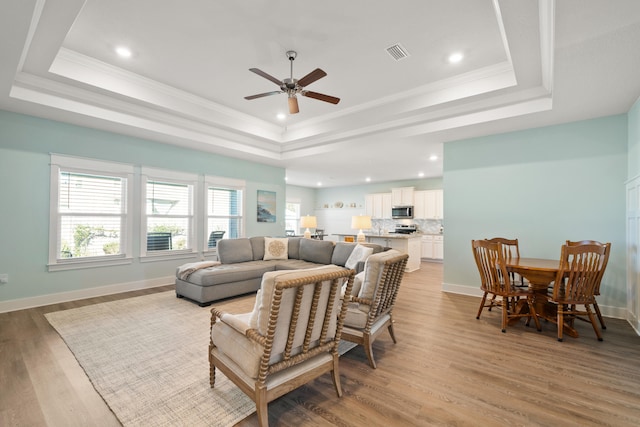 living room with ceiling fan, light hardwood / wood-style floors, and a raised ceiling