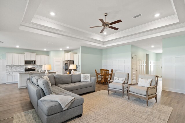 living room featuring ceiling fan, light wood-type flooring, crown molding, and a tray ceiling