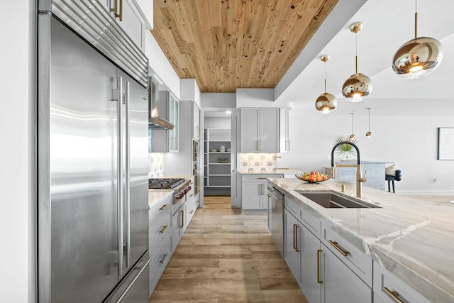 kitchen with pendant lighting, sink, light stone countertops, appliances with stainless steel finishes, and light hardwood / wood-style floors