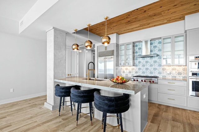 kitchen with a breakfast bar, light hardwood / wood-style flooring, wall chimney range hood, and appliances with stainless steel finishes