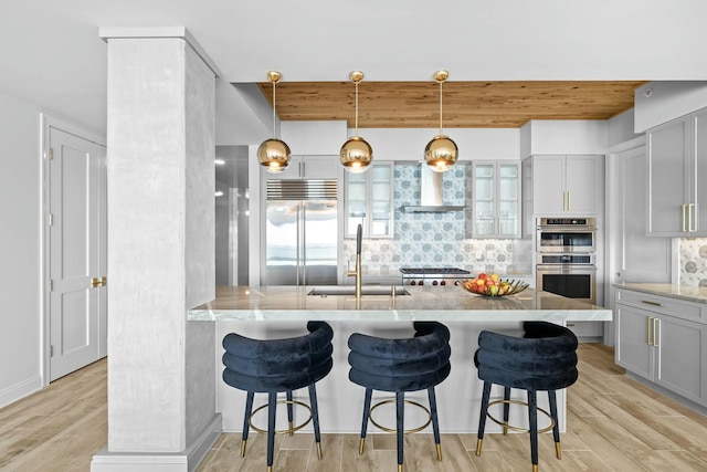 kitchen featuring appliances with stainless steel finishes, backsplash, wall chimney exhaust hood, sink, and light hardwood / wood-style flooring