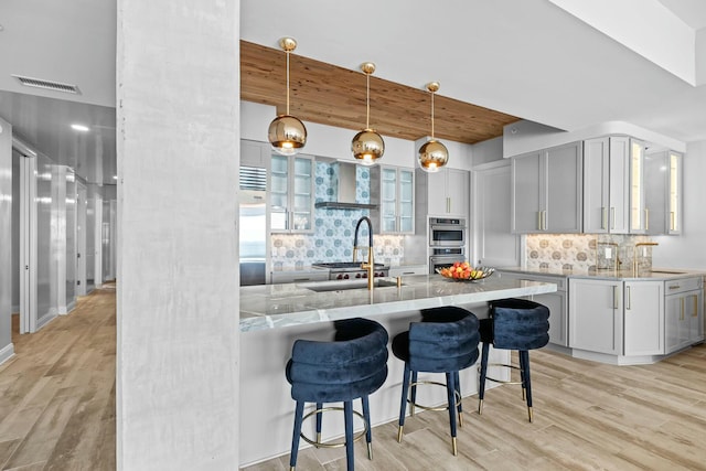 kitchen with decorative backsplash, light stone countertops, sink, pendant lighting, and light hardwood / wood-style flooring