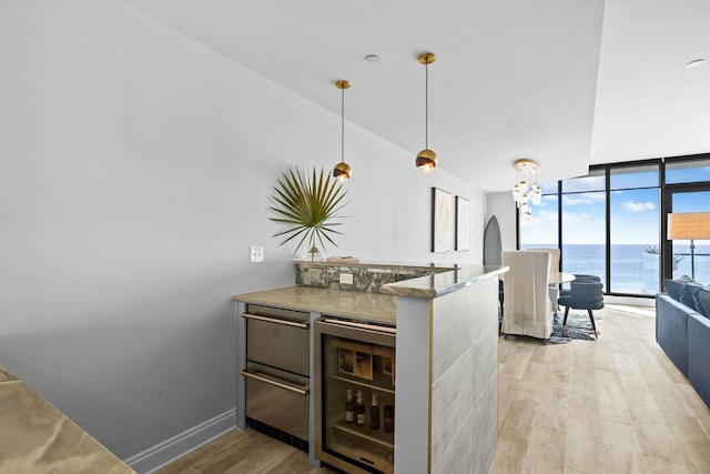 kitchen with hanging light fixtures, light wood-type flooring, a water view, and beverage cooler