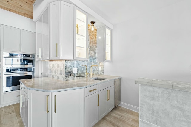 kitchen featuring white cabinetry, light wood-type flooring, stainless steel double oven, and sink