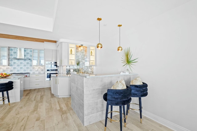 kitchen with a center island, wall chimney exhaust hood, a kitchen bar, white cabinets, and light wood-type flooring