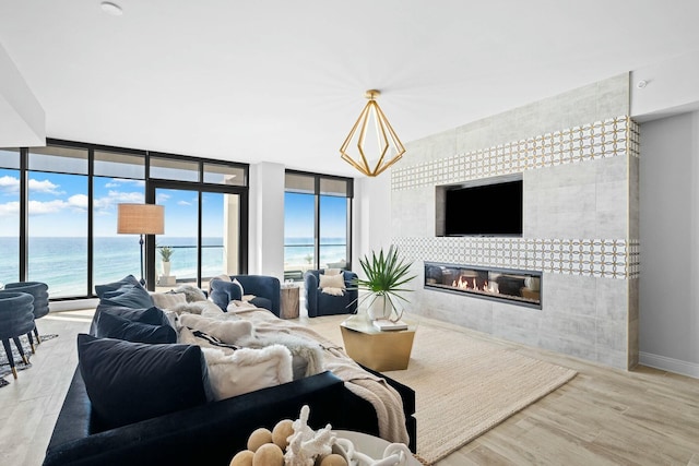 living room featuring a tile fireplace, a water view, light hardwood / wood-style floors, and expansive windows