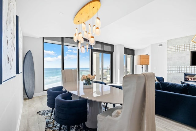 dining room with a notable chandelier, floor to ceiling windows, a water view, and light wood-type flooring