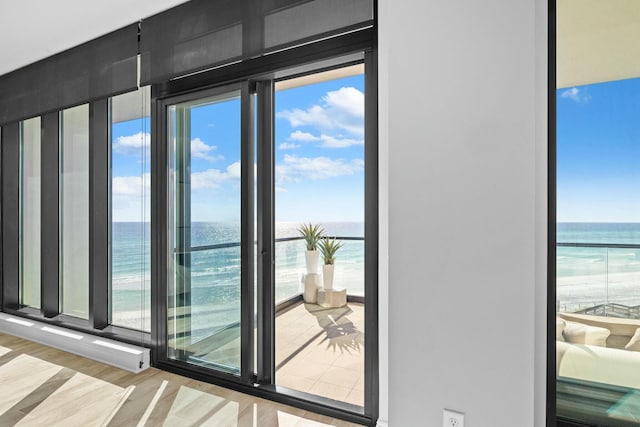 doorway to outside with a water view, light hardwood / wood-style floors, and a beach view