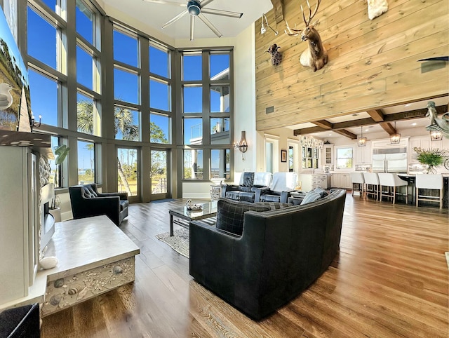 living room featuring a high ceiling, beam ceiling, ceiling fan, and wood-type flooring