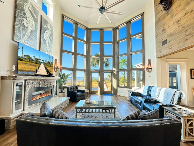 living room with ceiling fan, wood-type flooring, a towering ceiling, and a high end fireplace