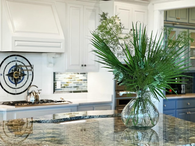 bar featuring stainless steel gas stovetop, white cabinetry, dark stone counters, and custom exhaust hood