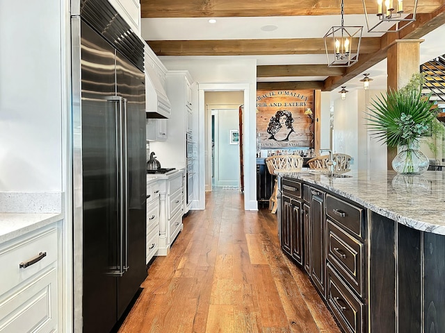 kitchen featuring beam ceiling, white cabinets, light hardwood / wood-style floors, and stainless steel built in refrigerator