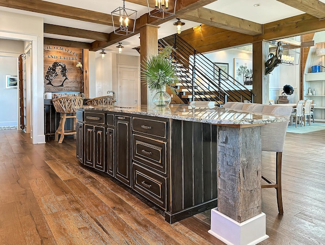 kitchen with beam ceiling, dark hardwood / wood-style flooring, pendant lighting, a breakfast bar, and a center island with sink