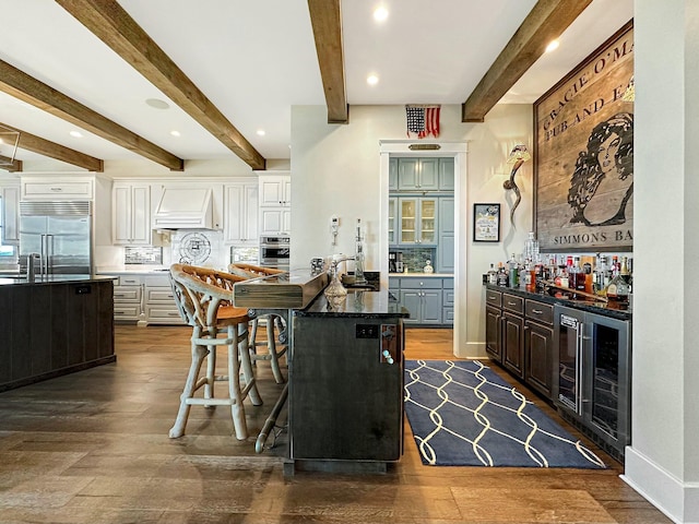 kitchen with white cabinets, a kitchen breakfast bar, a kitchen island, stainless steel appliances, and beverage cooler