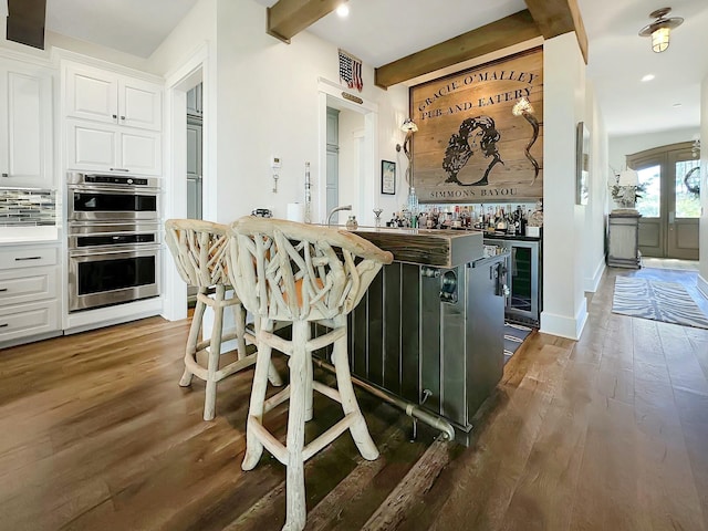 kitchen with white cabinetry, dark wood-type flooring, tasteful backsplash, a kitchen breakfast bar, and double oven