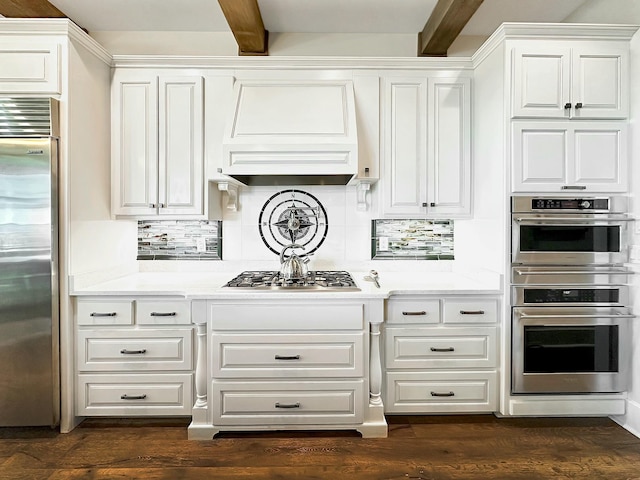 kitchen with appliances with stainless steel finishes, white cabinets, tasteful backsplash, custom range hood, and beamed ceiling