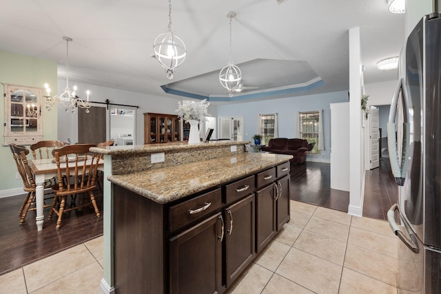 kitchen featuring stainless steel fridge, a barn door, decorative light fixtures, light hardwood / wood-style floors, and dark brown cabinetry