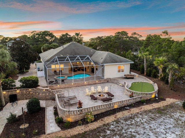 back house at dusk with a fire pit, a lanai, and a patio area