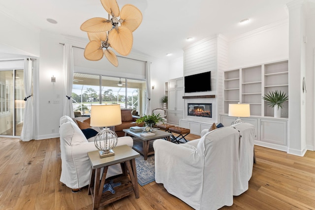 living room featuring a tiled fireplace, crown molding, and light hardwood / wood-style flooring