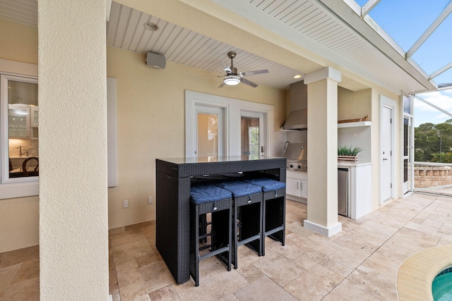 view of patio with ceiling fan, exterior kitchen, and glass enclosure