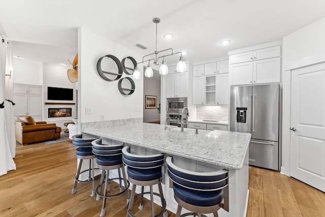 kitchen with white cabinets, hanging light fixtures, light wood-type flooring, kitchen peninsula, and stainless steel appliances