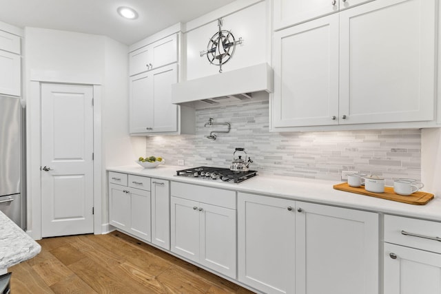 kitchen with decorative backsplash, appliances with stainless steel finishes, custom range hood, light hardwood / wood-style floors, and white cabinetry