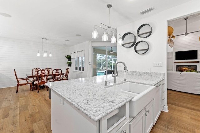 kitchen featuring sink, hanging light fixtures, wood walls, white cabinets, and light wood-type flooring