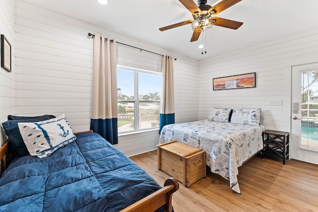 bedroom with hardwood / wood-style flooring, ceiling fan, wood walls, and multiple windows