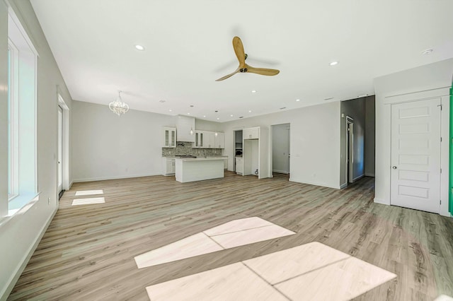 unfurnished living room with ceiling fan with notable chandelier and light hardwood / wood-style flooring