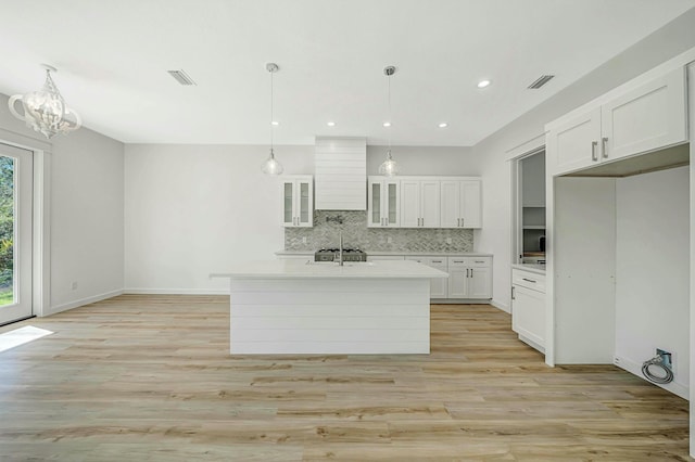 kitchen with white cabinetry, pendant lighting, and a kitchen island with sink