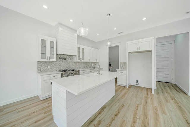 kitchen featuring light wood-type flooring, white cabinetry, high end stainless steel range oven, and an island with sink