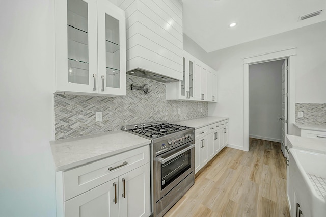 kitchen with backsplash, light hardwood / wood-style flooring, stainless steel range, white cabinetry, and custom range hood