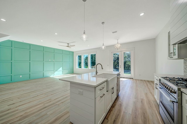 kitchen featuring a kitchen island with sink, sink, high end stainless steel range, light wood-type flooring, and white cabinetry