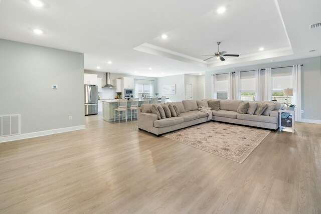 living room featuring a raised ceiling, ceiling fan, and light wood-type flooring