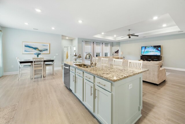 kitchen featuring dishwasher, sink, ceiling fan, an island with sink, and light stone counters